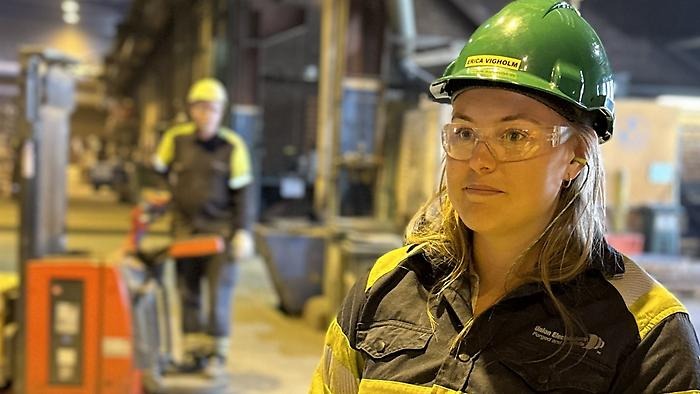 Kvinna med hjälm och skyddsglasögon med fabriken i bakgrunden