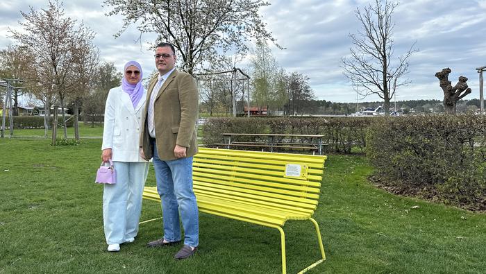 En kvinna och en man står framför en gul bänk. 